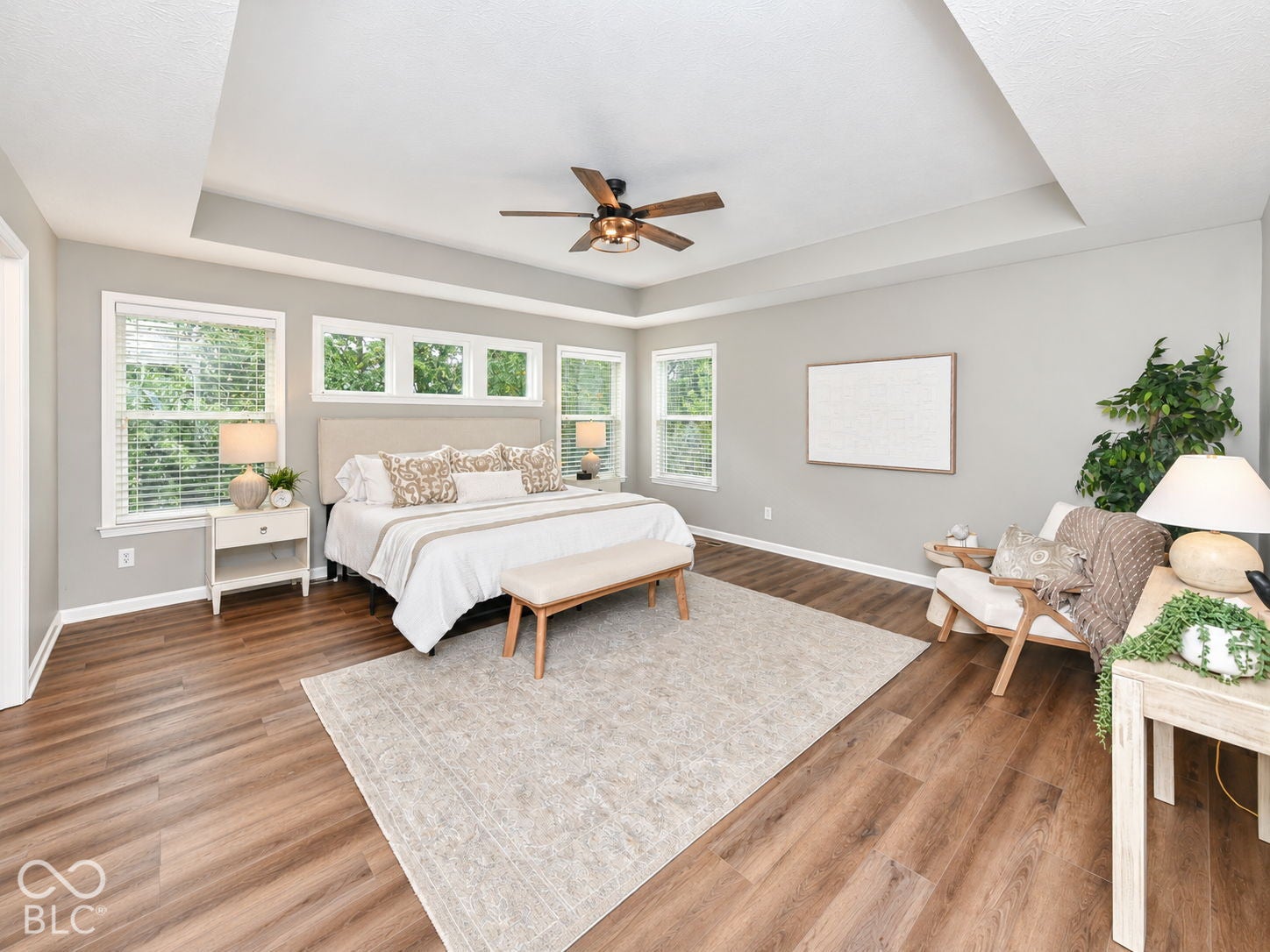 Tray ceiling with a ceiling fan, wood-finish flooring, multiple windows with blinds, and light gray wall paint