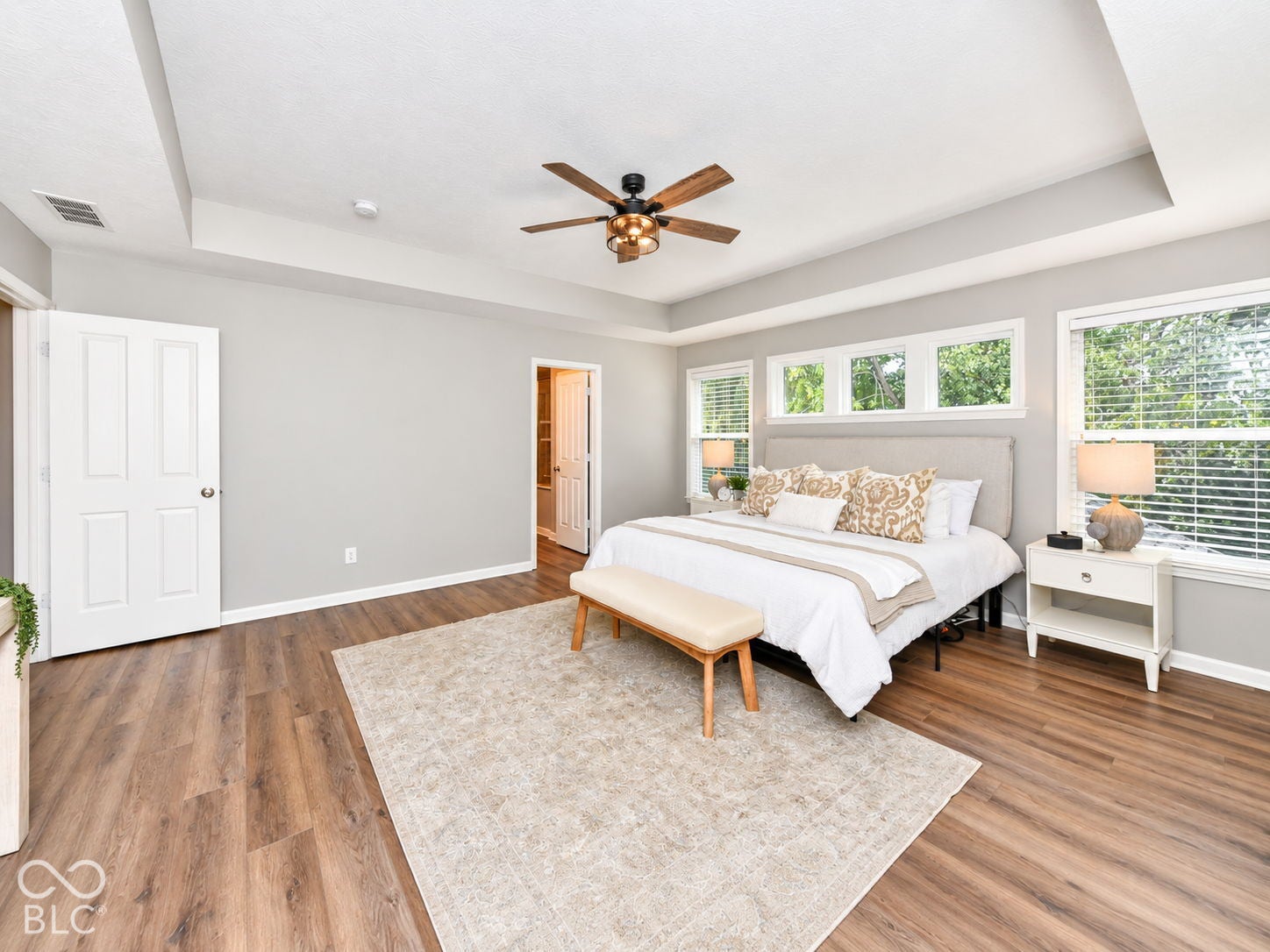 Tray ceiling, wood-finish flooring, abundant natural light, ceiling fan, and white trim