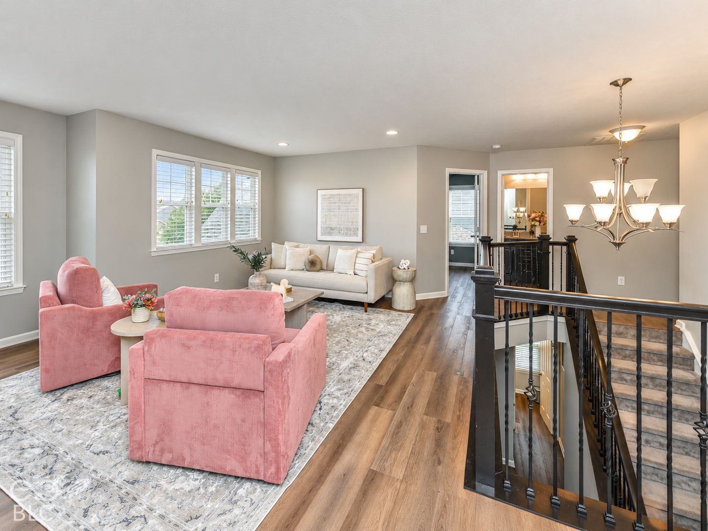 Upper-level living area featuring wood-finish flooring, multiple windows with blinds, and a built-in chandelier