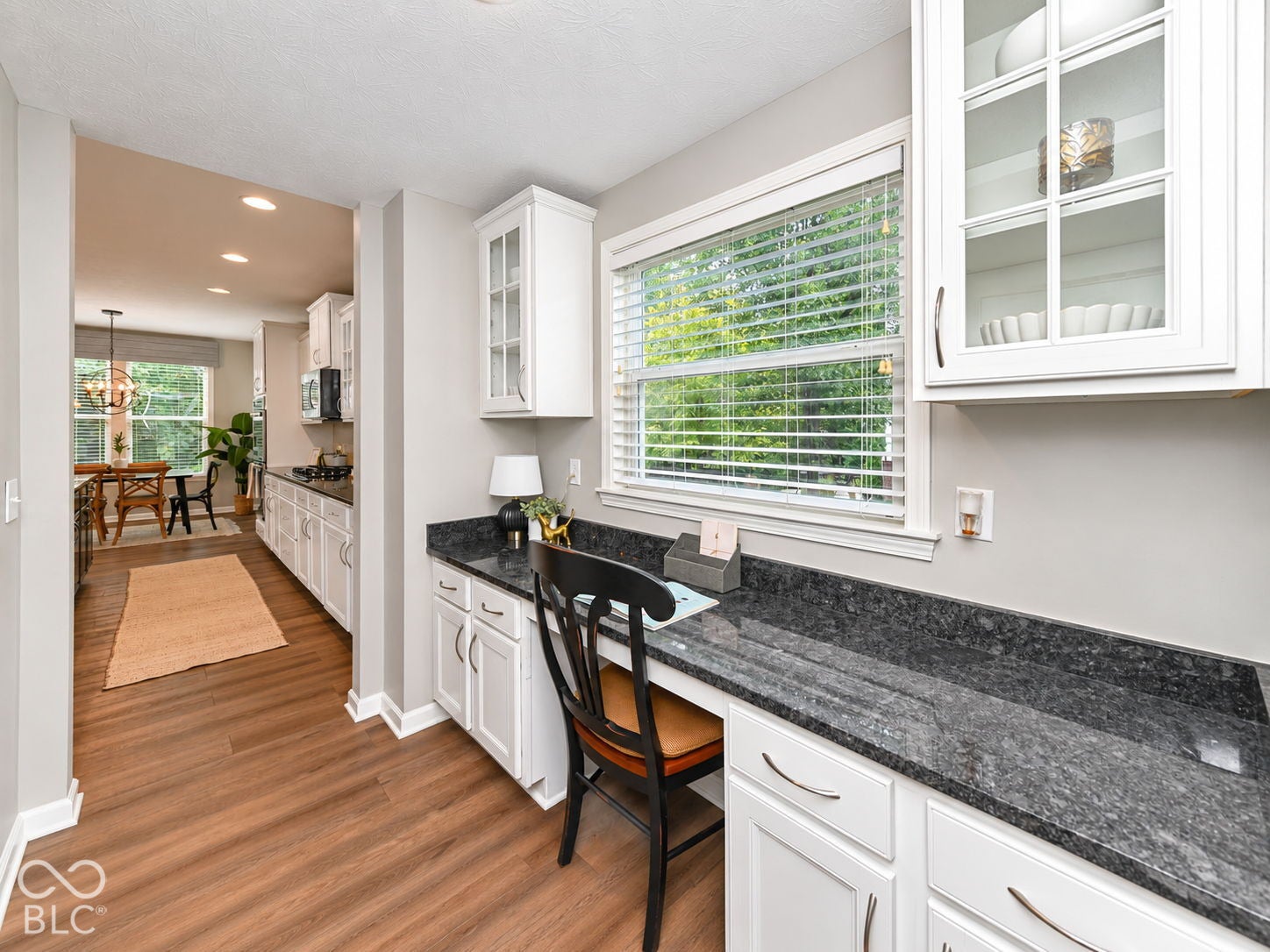 Built-in desk area with a dark speckled countertop, white cabinetry with glass-front uppers, and wood-finish flooring