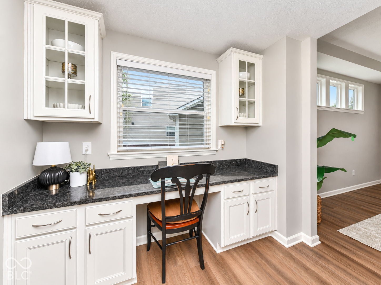 Built-in desk area with dark countertop, white shaker-style cabinetry, and wood-finish flooring