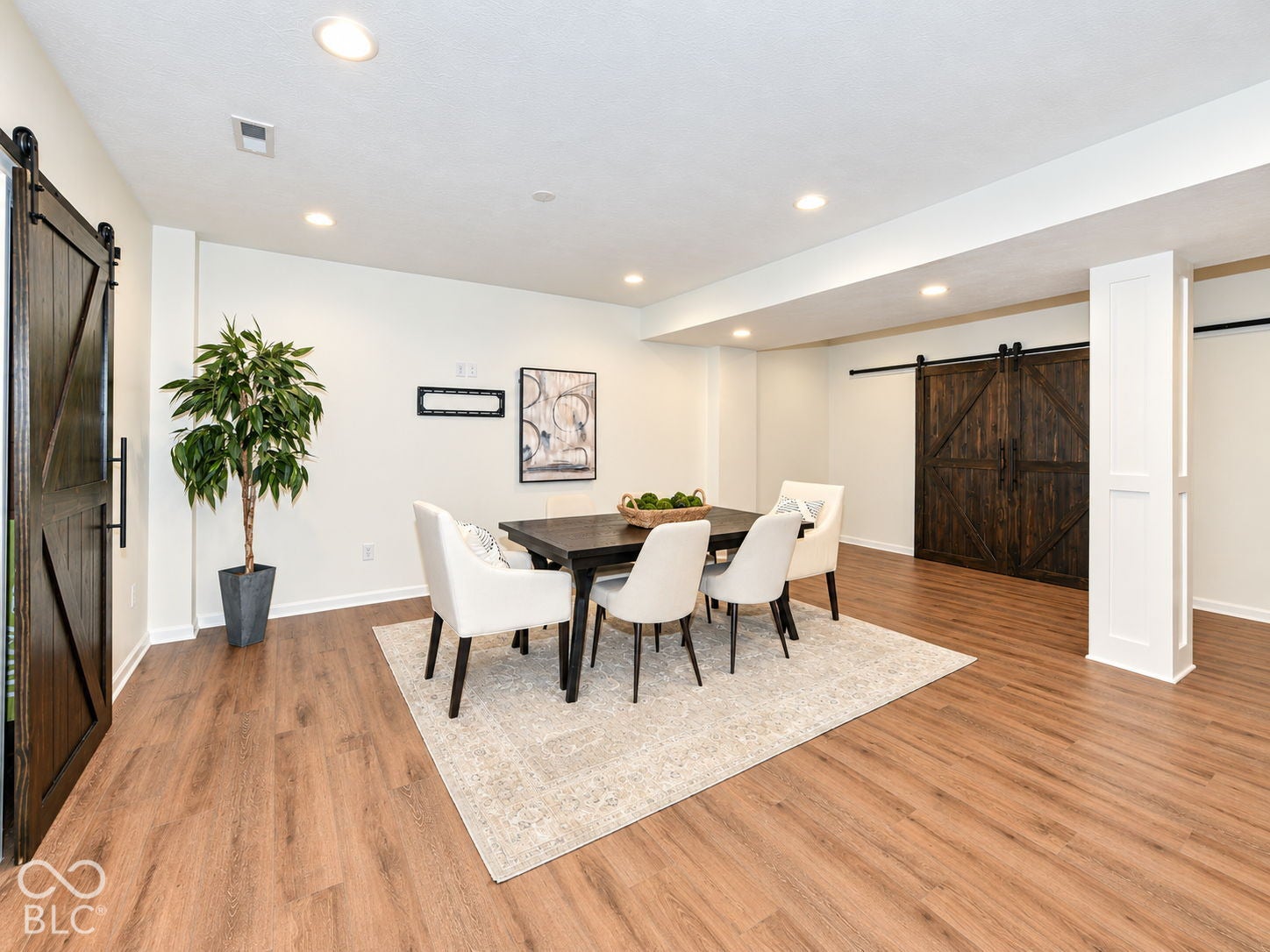Wood-finish flooring throughout, recessed ceiling lighting, and two dark wood barn doors with black hardware