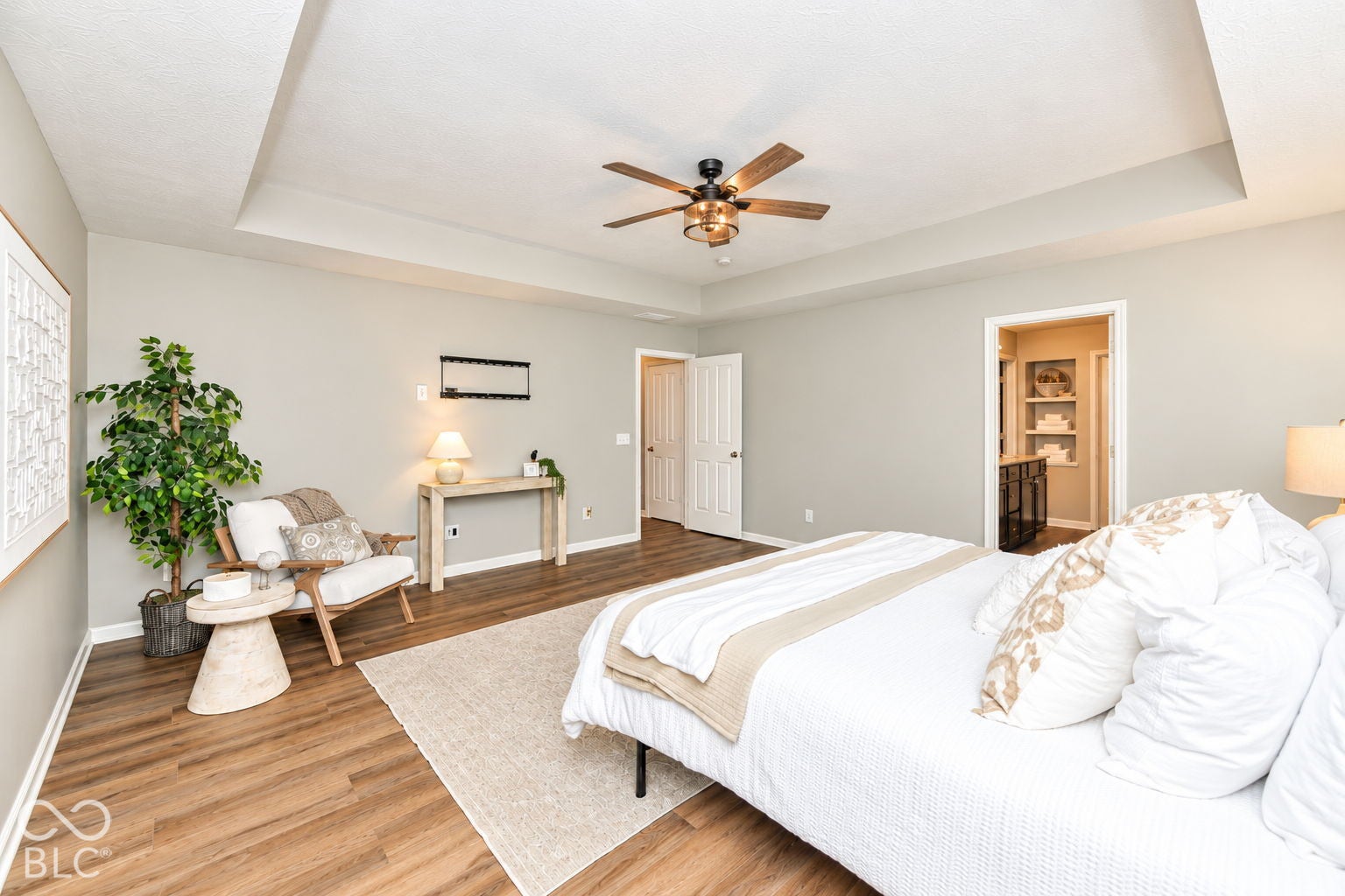 Tray ceiling, wood-finish flooring, ceiling fan with integrated lighting, recessed door, and built-in shelving