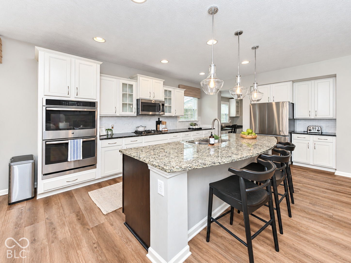 Kitchen featuring white cabinetry, wood-finish flooring, stainless steel appliances, a center island with a stone countertop, and pendant lighting