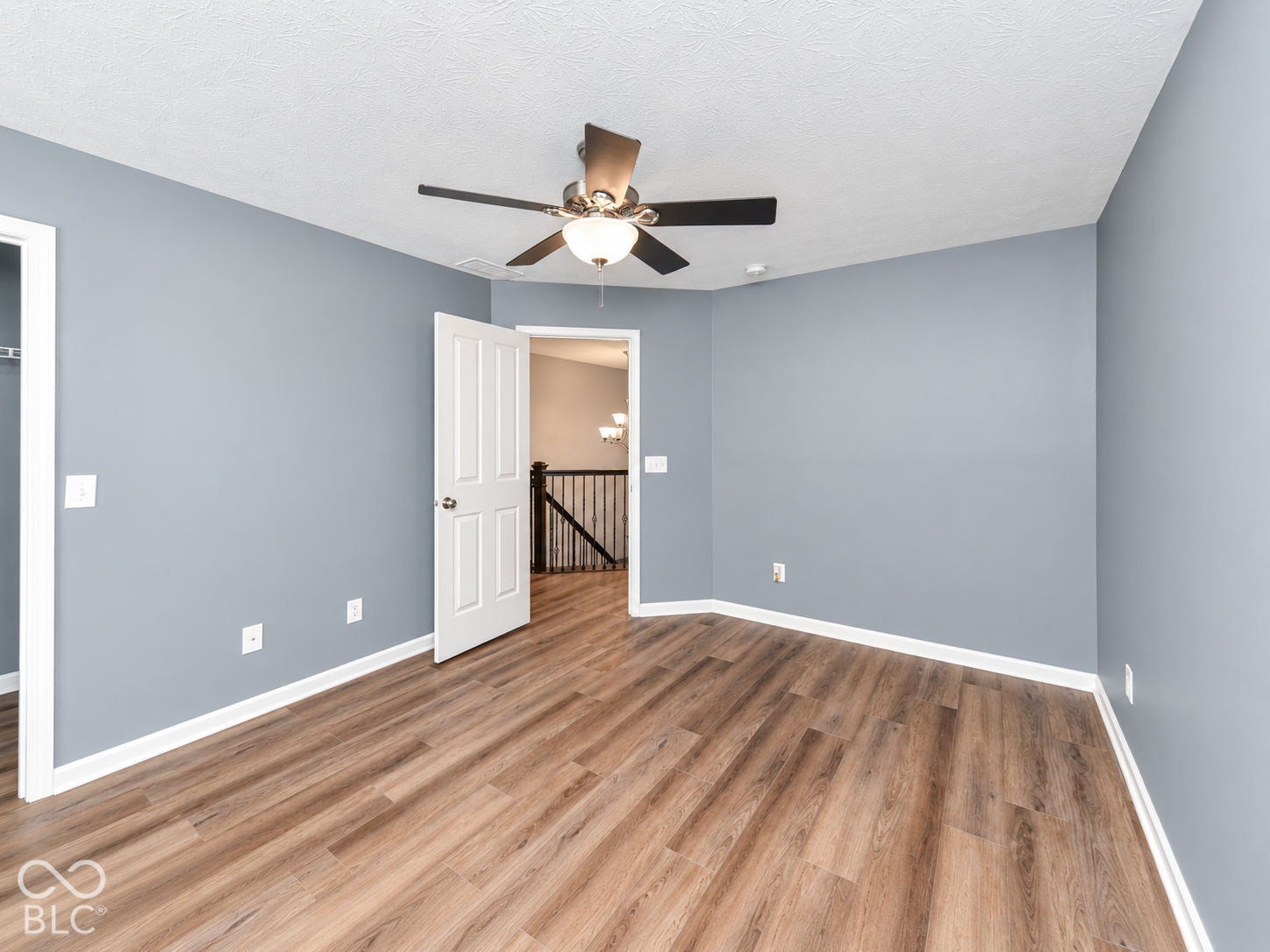 Wood-finish flooring, ceiling fan with integrated lighting, paneled interior door, and white trim