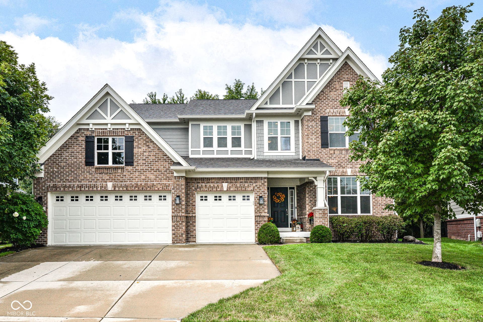 Brick and siding exterior, multi-gabled roofline, two-car garage, covered entry porch with columns, established landscaping