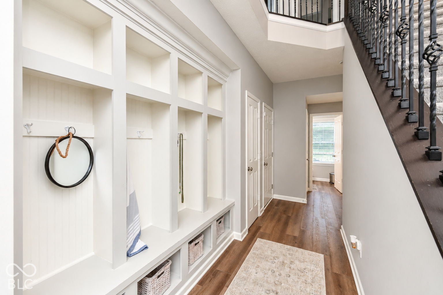 Built-in organizational shelving with integrated seating, wood-finish flooring, and a staircase with decorative wrought iron balusters