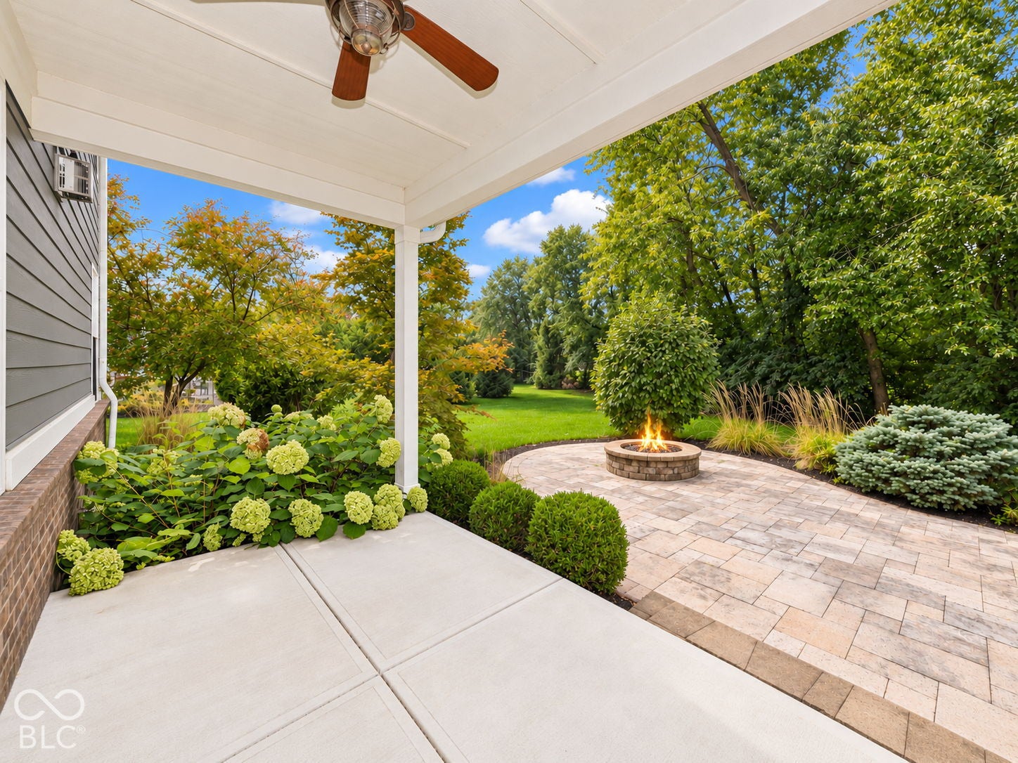 Covered patio featuring a ceiling fan, a paved fire pit area, and mature landscaping