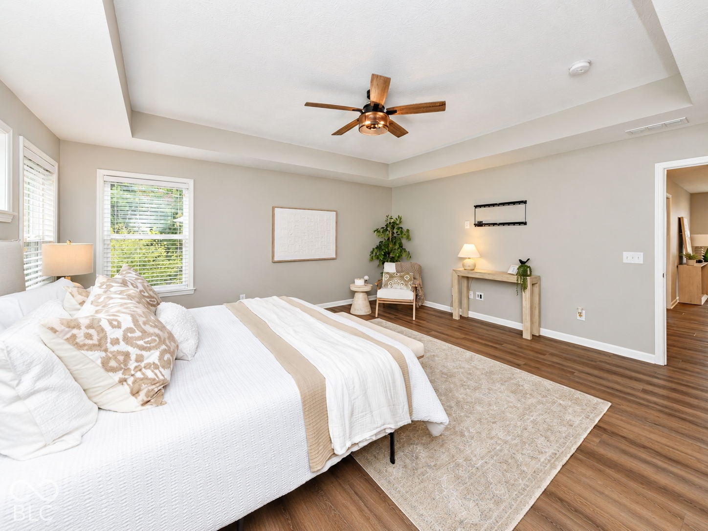Tray ceiling with a ceiling fan, wood-finish flooring, two windows with blinds, and a wide entryway