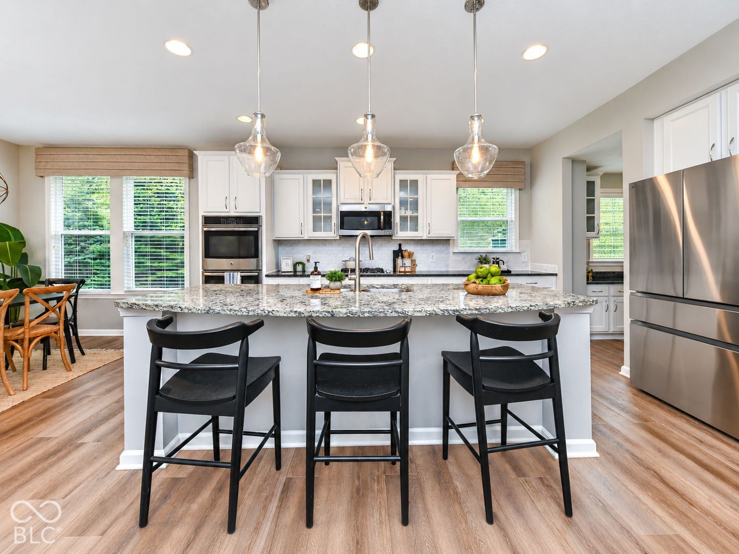 White cabinetry, stainless steel appliances, wood-finish flooring, recessed lighting, and a large central island with seating