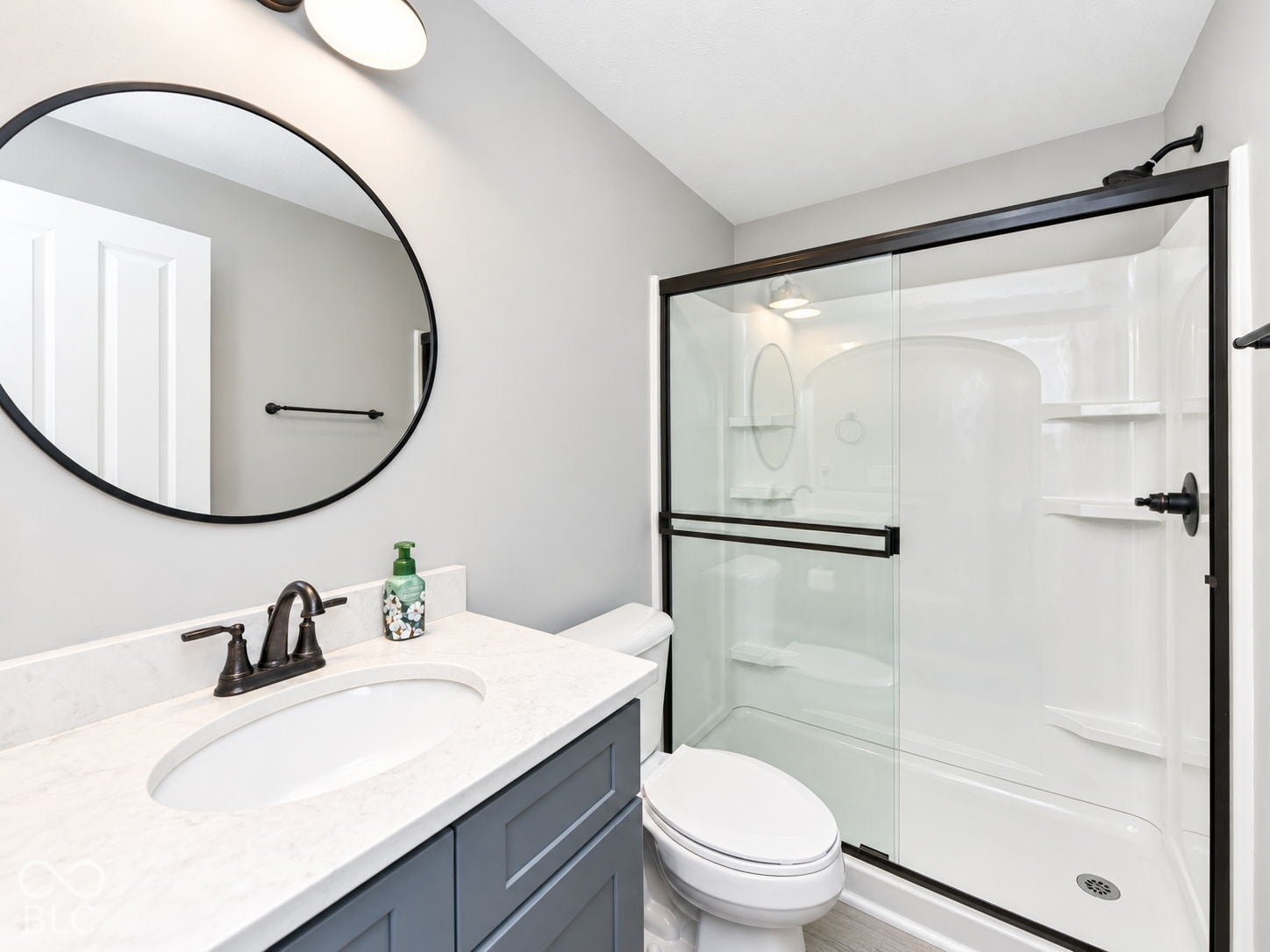 Bathroom featuring a vanity with an integrated sink, a dark bronze faucet, a round wall mirror, and a shower with a sliding glass door