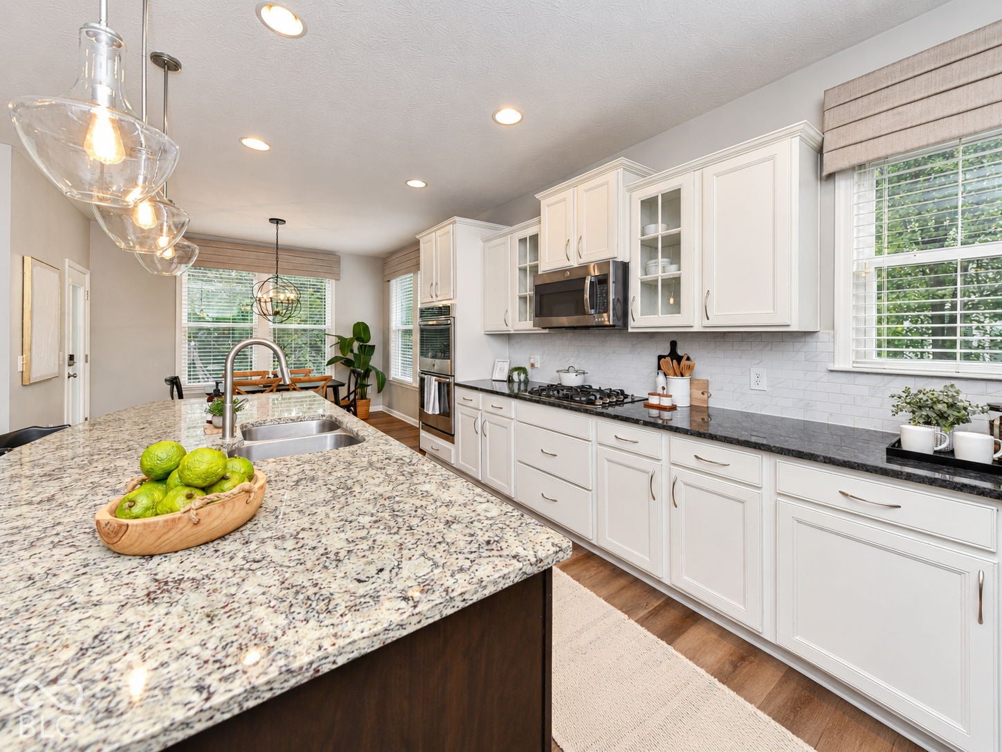 Kitchen island with granite countertop and undermount sink, stainless steel appliances, white cabinetry with glass-front accents, and wood-finish flooring