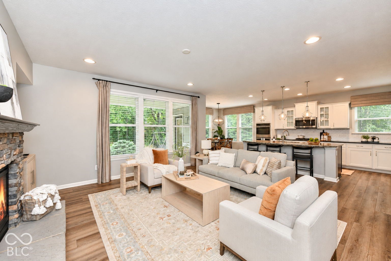 Open-concept living space featuring wood-finish flooring, a stone-clad fireplace, and recessed lighting