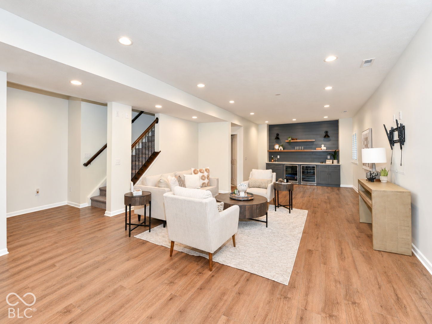 Wood-finish flooring throughout, recessed lighting, built-in wet bar with dual beverage refrigerators, shiplap accent wall, and staircase with dark wood handrails