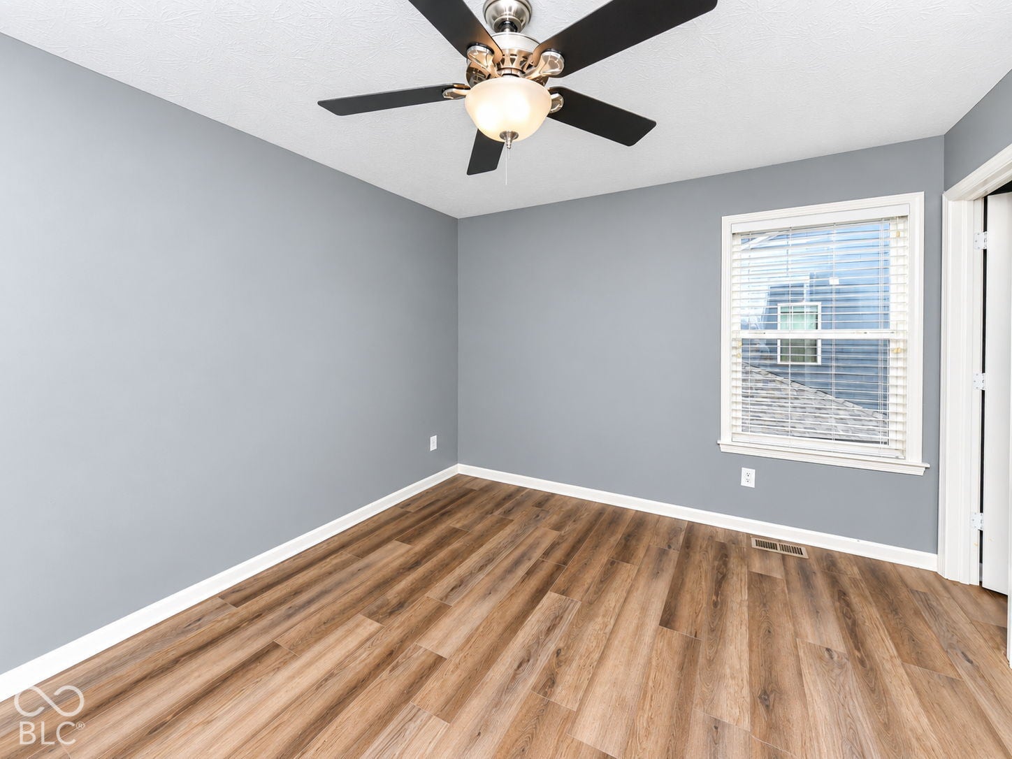 Wood-finish flooring, light grey wall paint, ceiling fan with integrated lighting, white window trim, and white baseboards