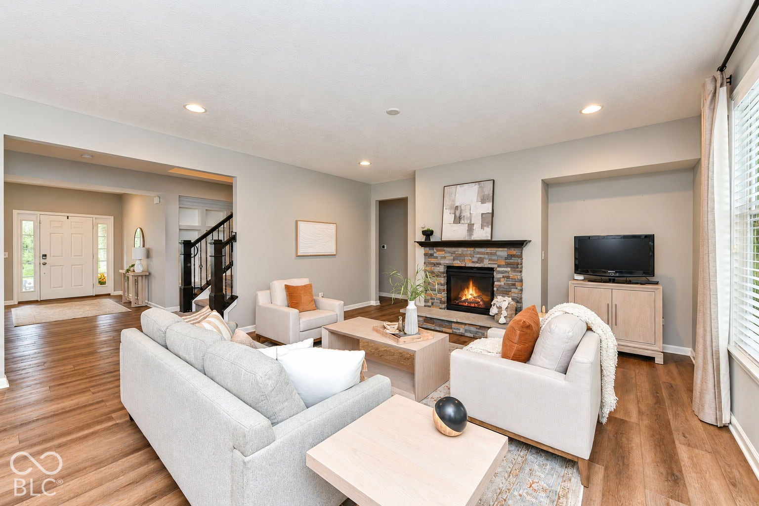 Spacious living area featuring wood-finish flooring, a stone-surround fireplace with a dark wood mantel, and recessed lighting
