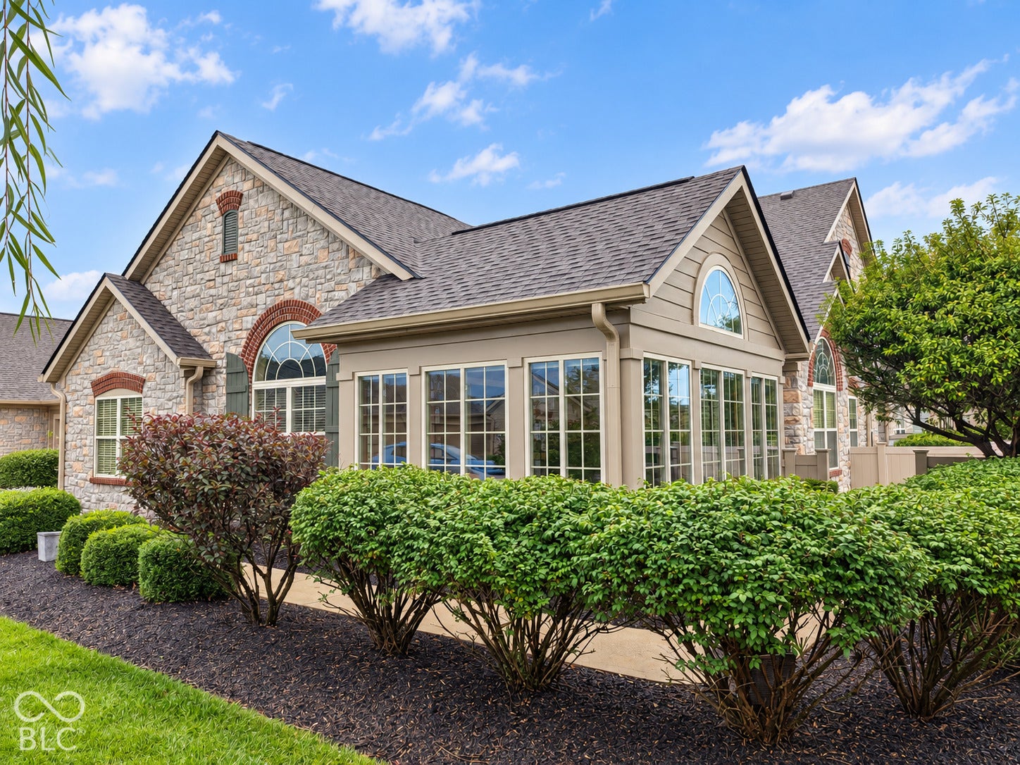 Stone exterior with arched windows, prominent sunroom with multiple windows, and a gabled roof