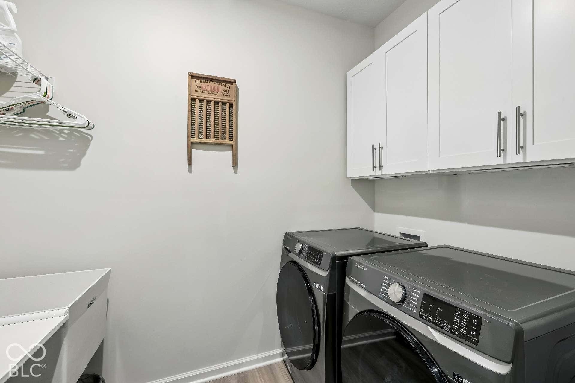 Upper white cabinetry with brushed nickel hardware, front-loading appliances, and wood-finish flooring