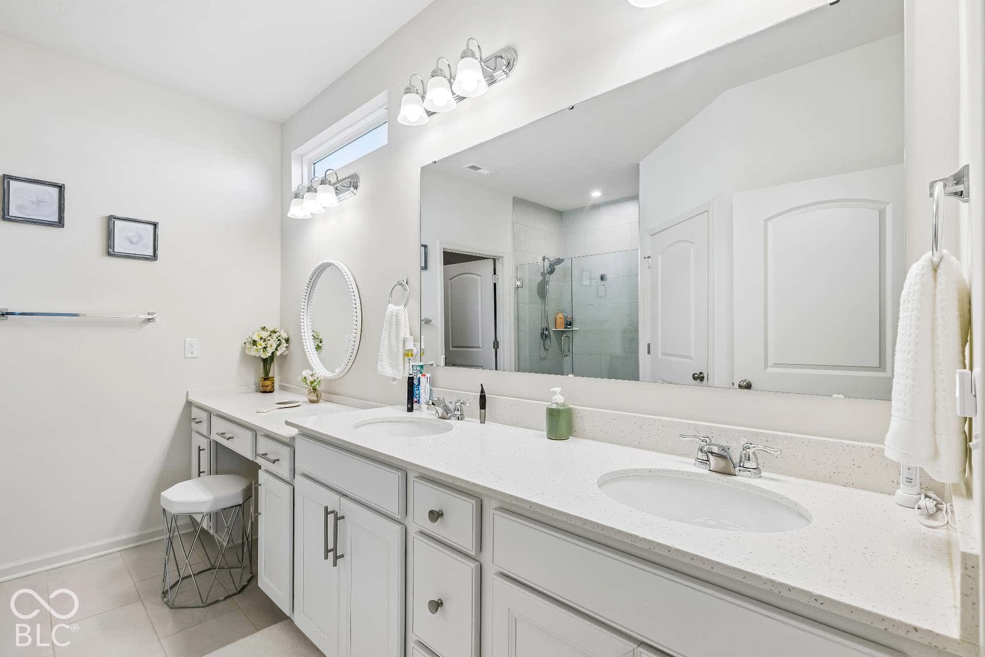 Dual vanity with integrated sinks and chrome fixtures, extensive countertop space, expansive wall mirror, and dedicated vanity area