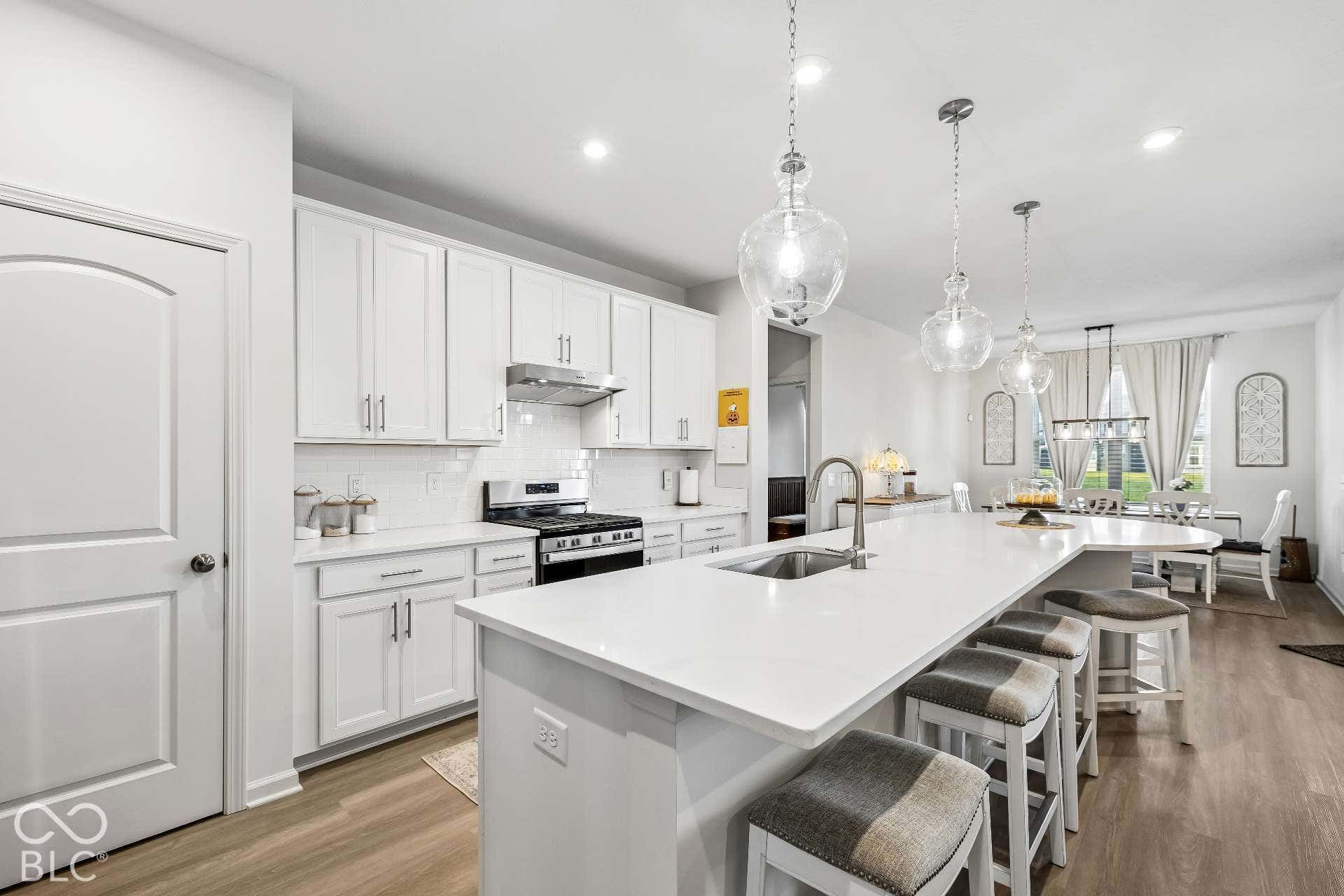Kitchen featuring white cabinetry, a large center island with integrated sink, stainless steel appliances, wood-finish flooring, and pendant lighting