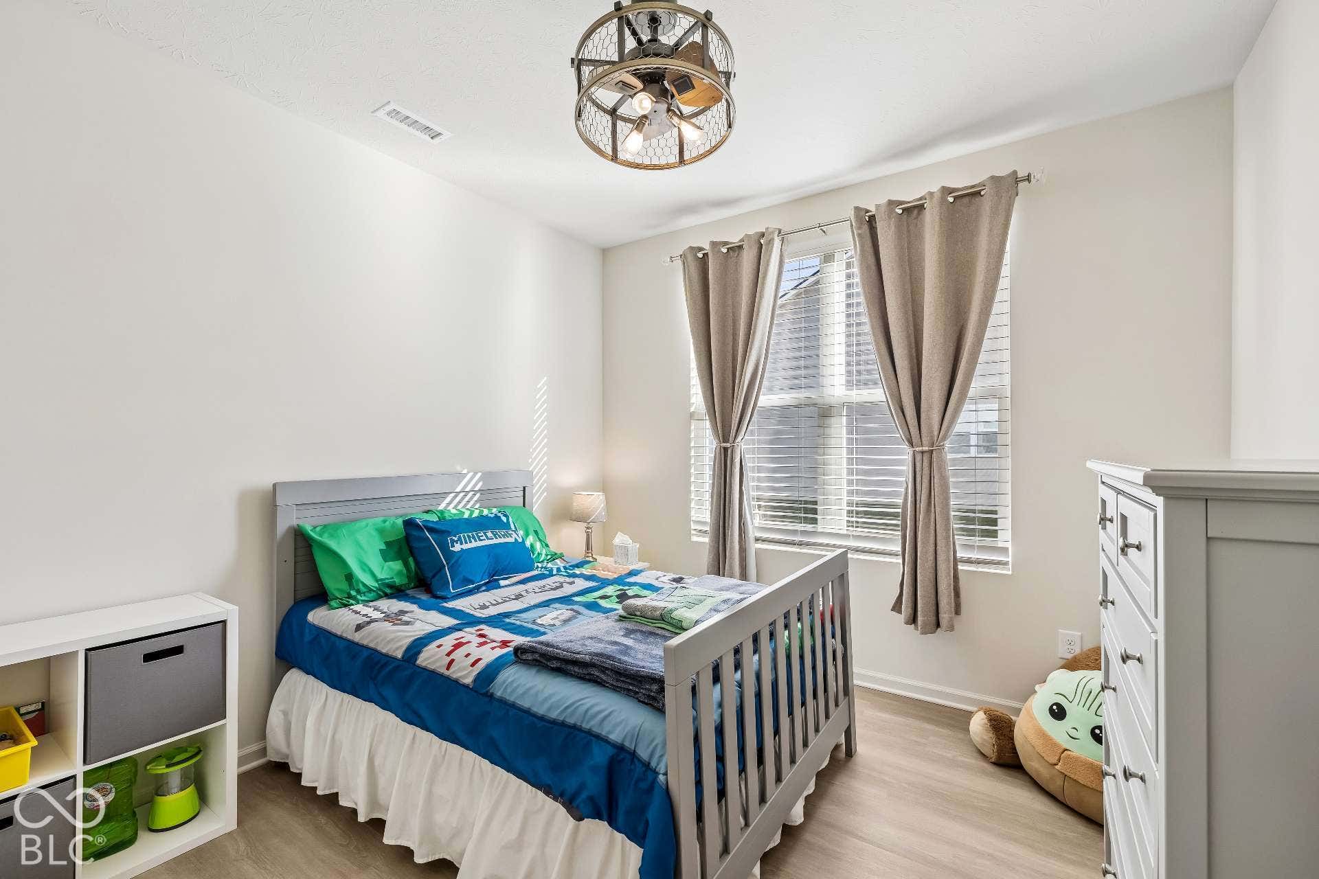 Wood-finish flooring, white walls, and a window with blinds and curtains