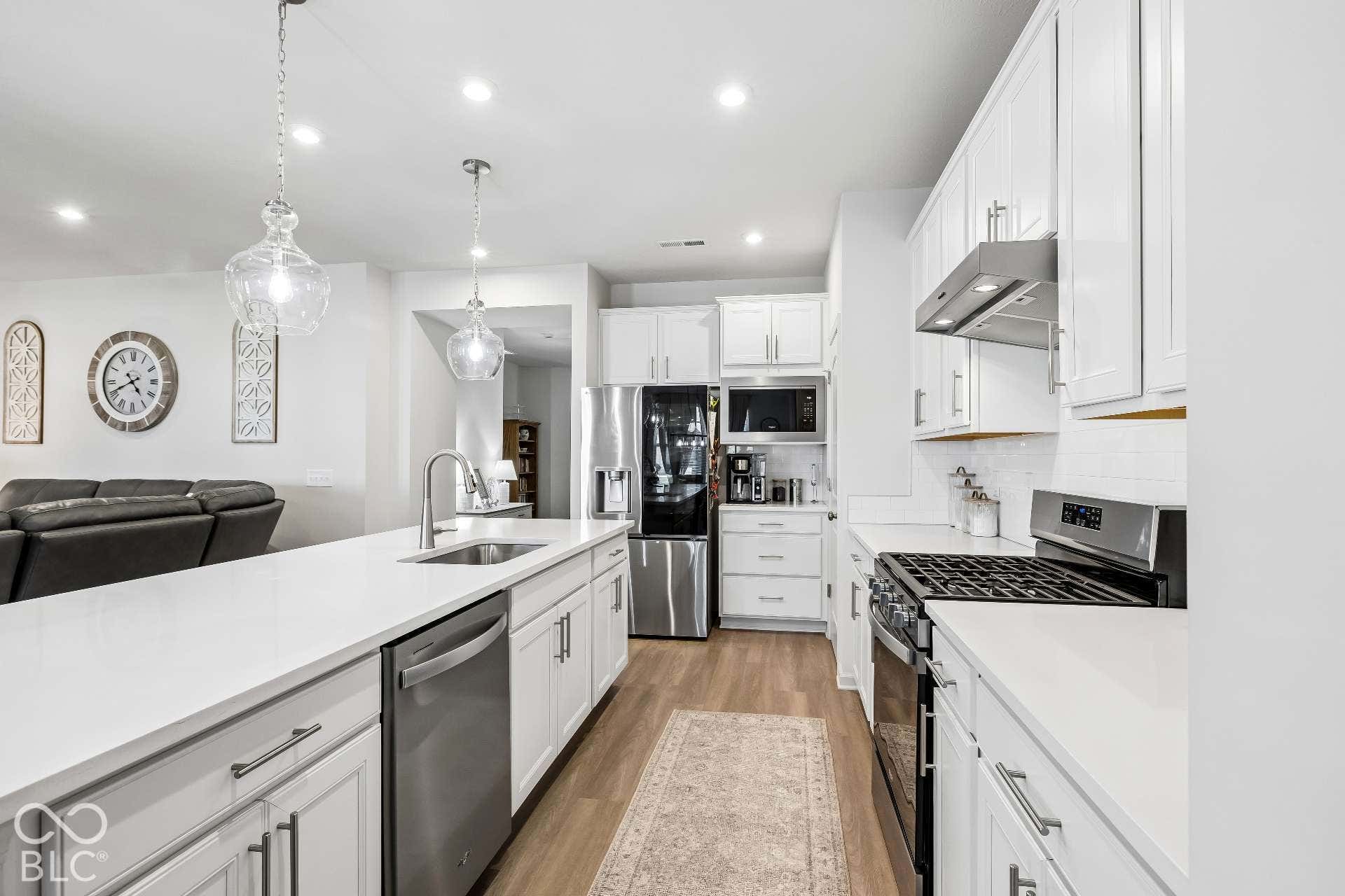 Kitchen featuring white cabinetry, stainless steel appliances, a center island with sink, and wood-finish flooring