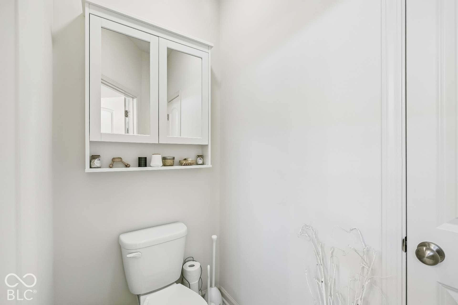 White wall-mounted medicine cabinet with mirrored doors, integrated open shelving, and a white two-piece toilet