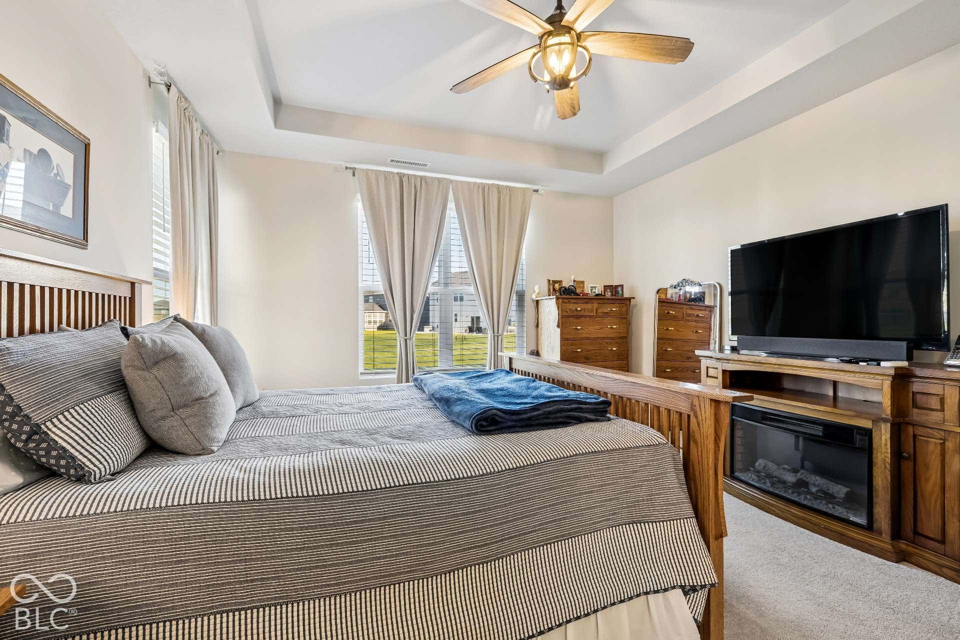 Tray ceiling with a decorative ceiling fan, light-colored walls, multiple windows with blinds, and wood-finish flooring