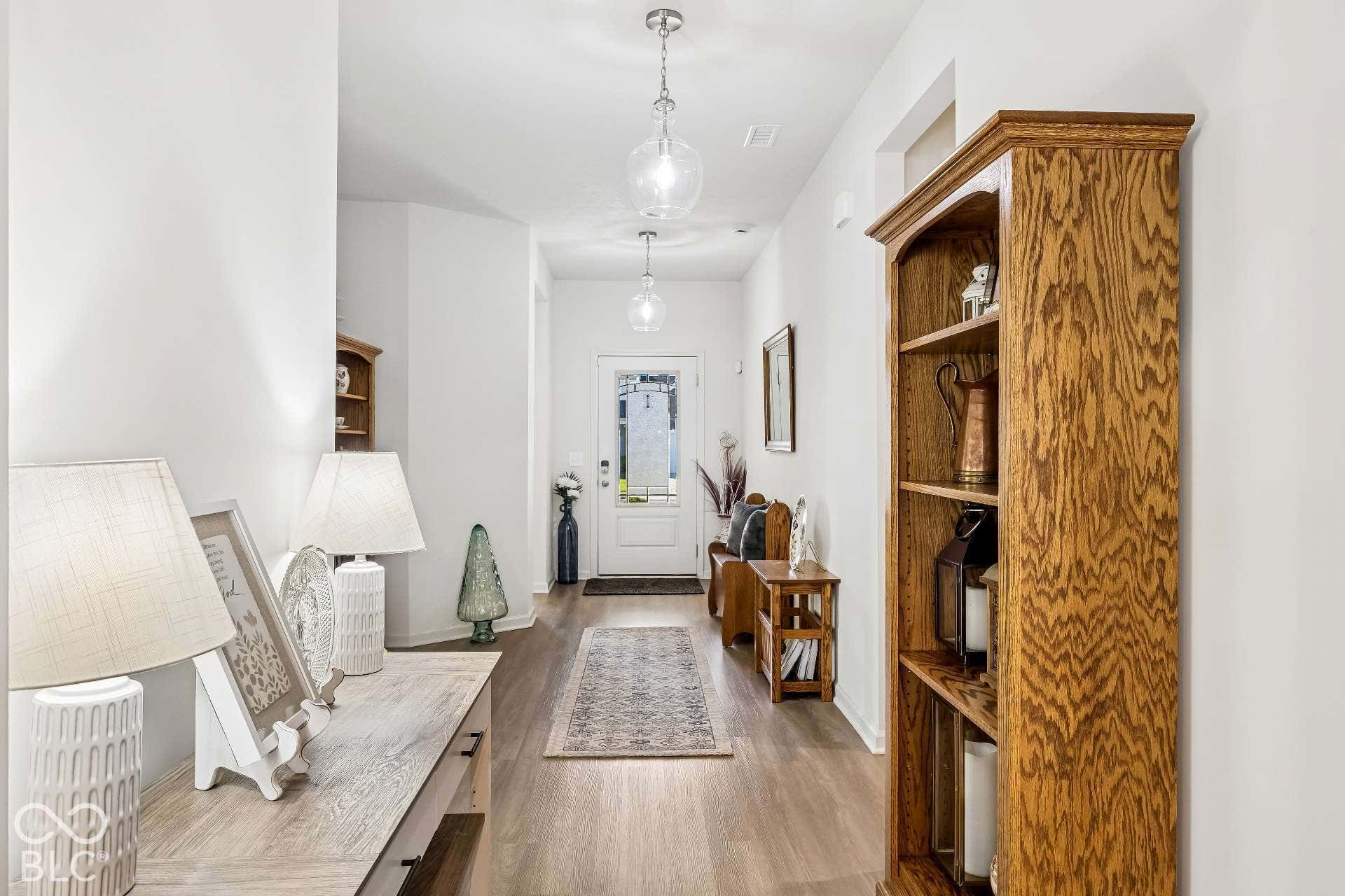 Hallway featuring wood-finish flooring, white walls, two hanging glass globe light fixtures, and a white paneled entry door