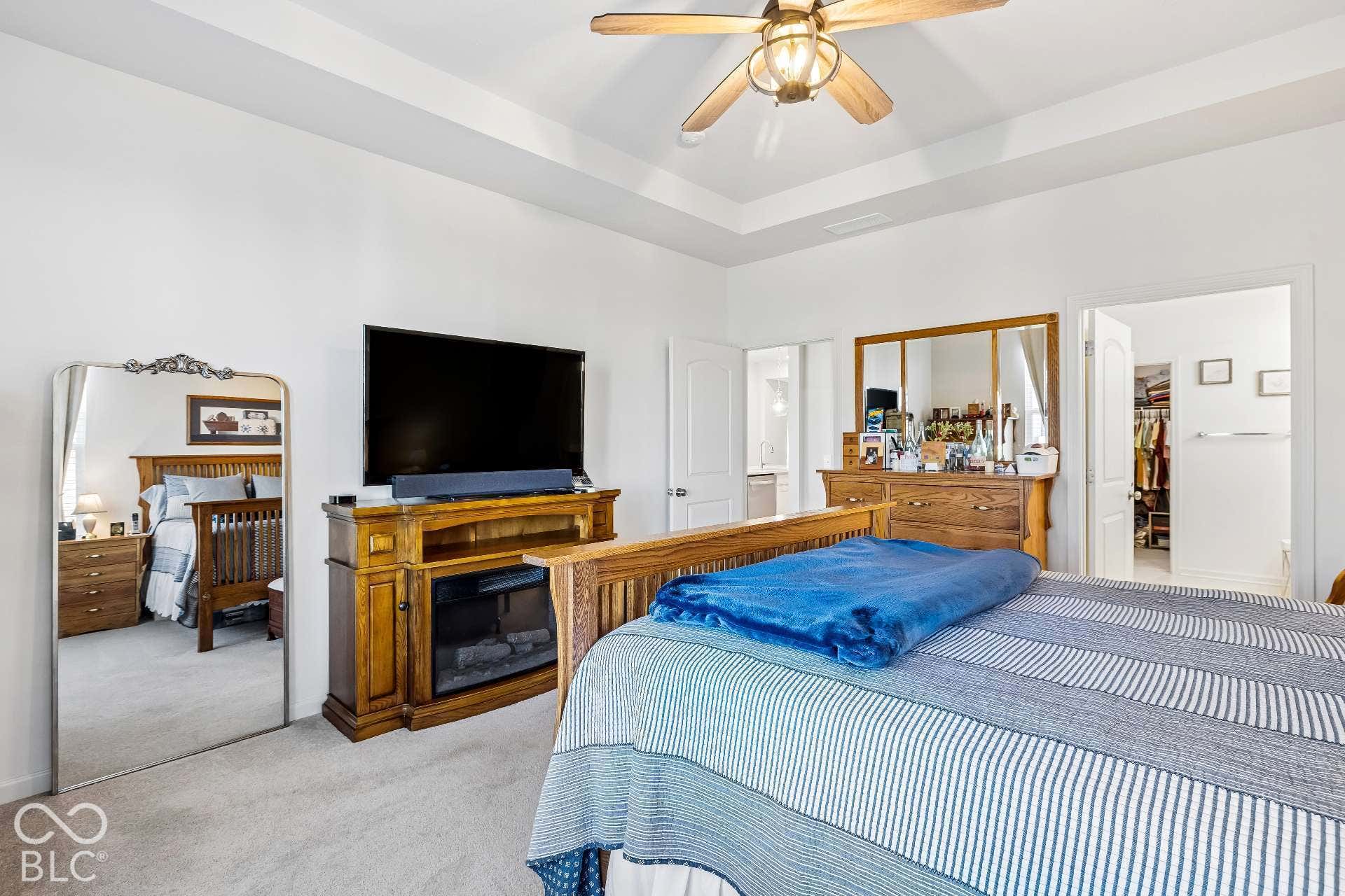 Tray ceiling with recessed lighting, ceiling fan with integrated lighting, wood-finish media console with electric fireplace insert, and plush carpet flooring
