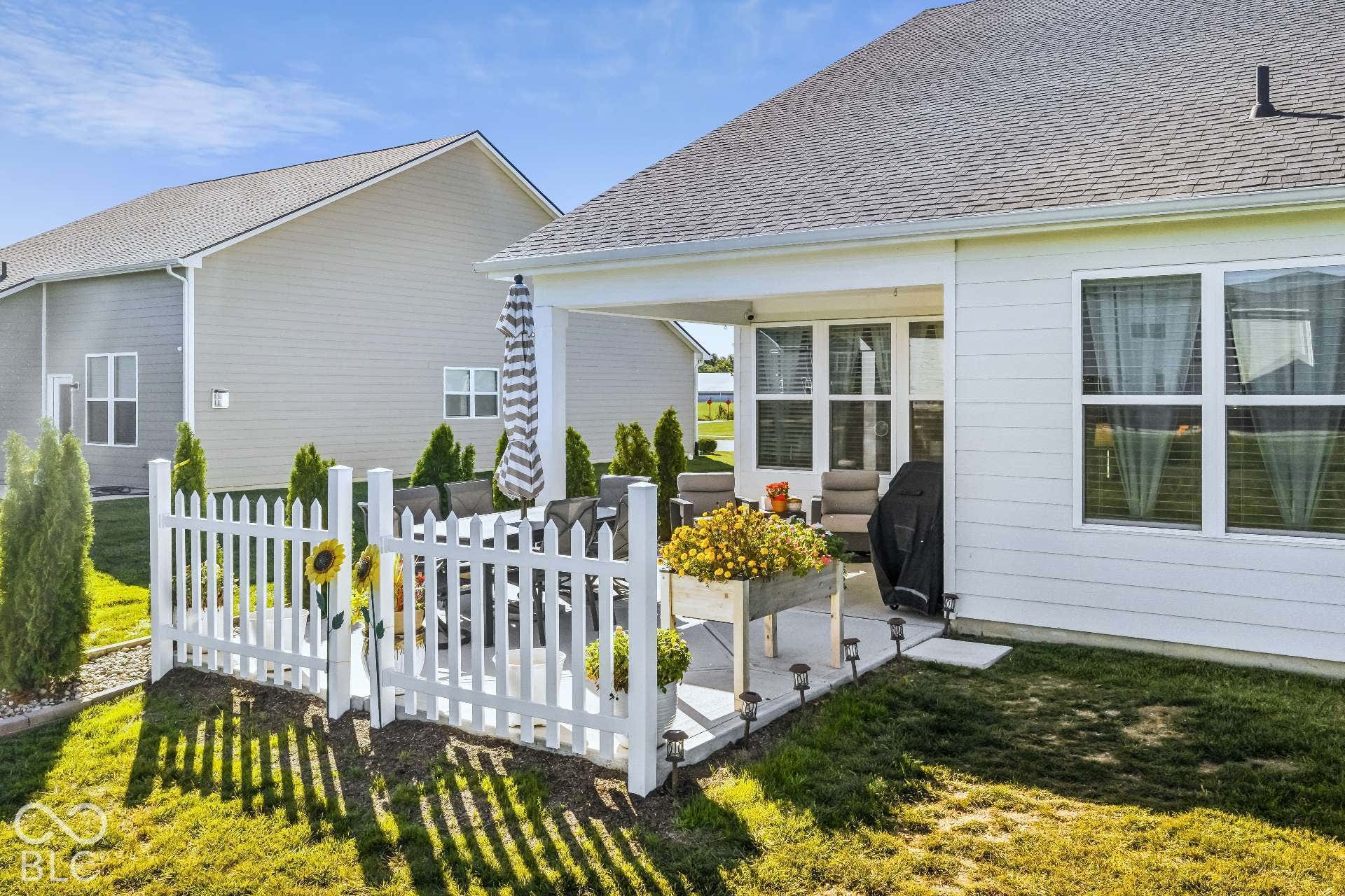 Covered patio with a white picket fence and surrounding lawn