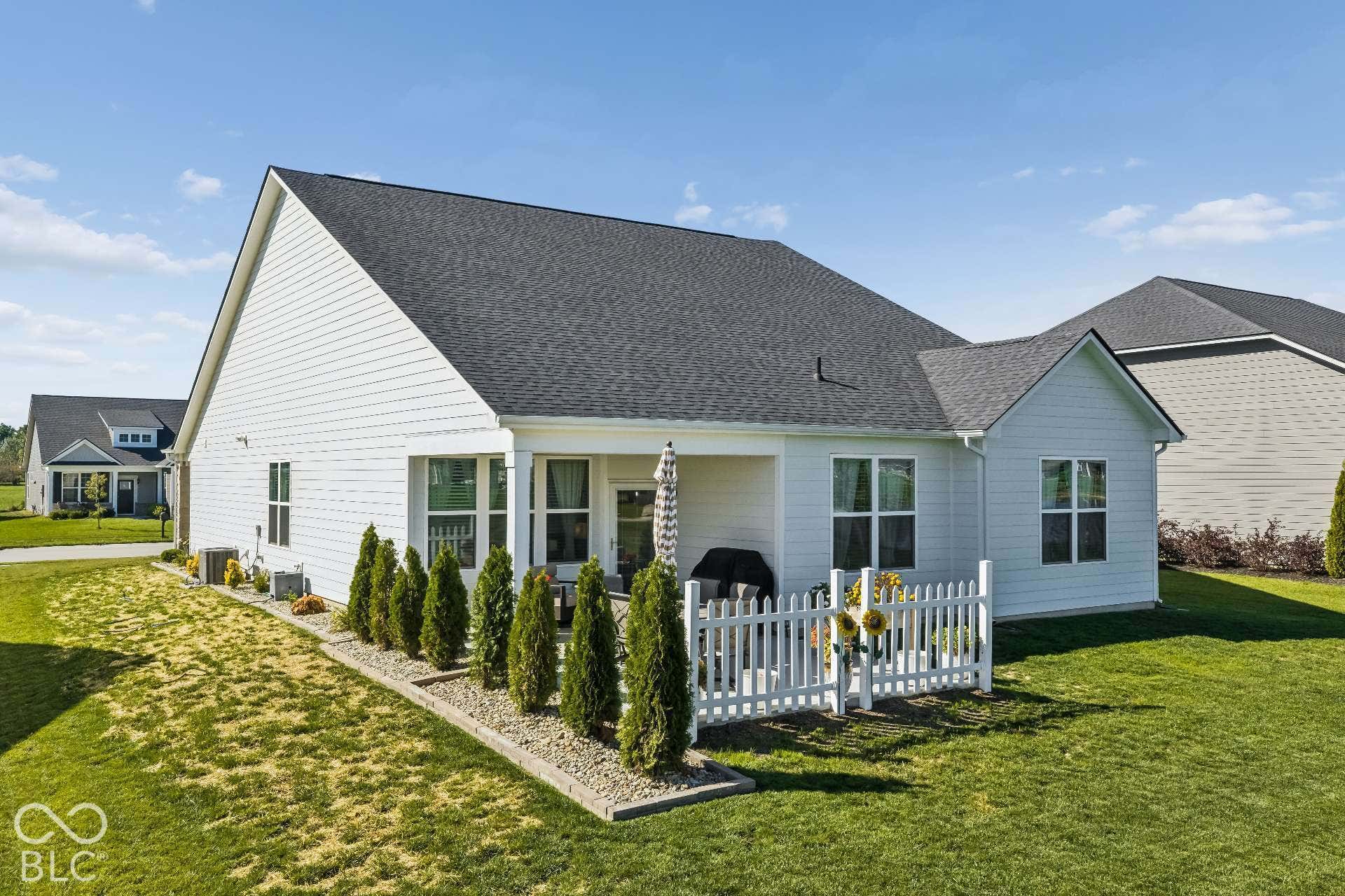 Charming farmhouse-style residence featuring a crisp white exterior with dark gray asphalt shingle roofing, gabled architectural details, and a welcoming front porch with white picket railing