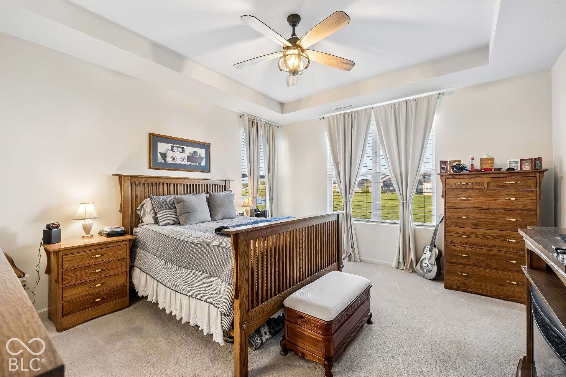 Tray ceiling with a ceiling fan light fixture, recessed windows, and soft neutral wall tones