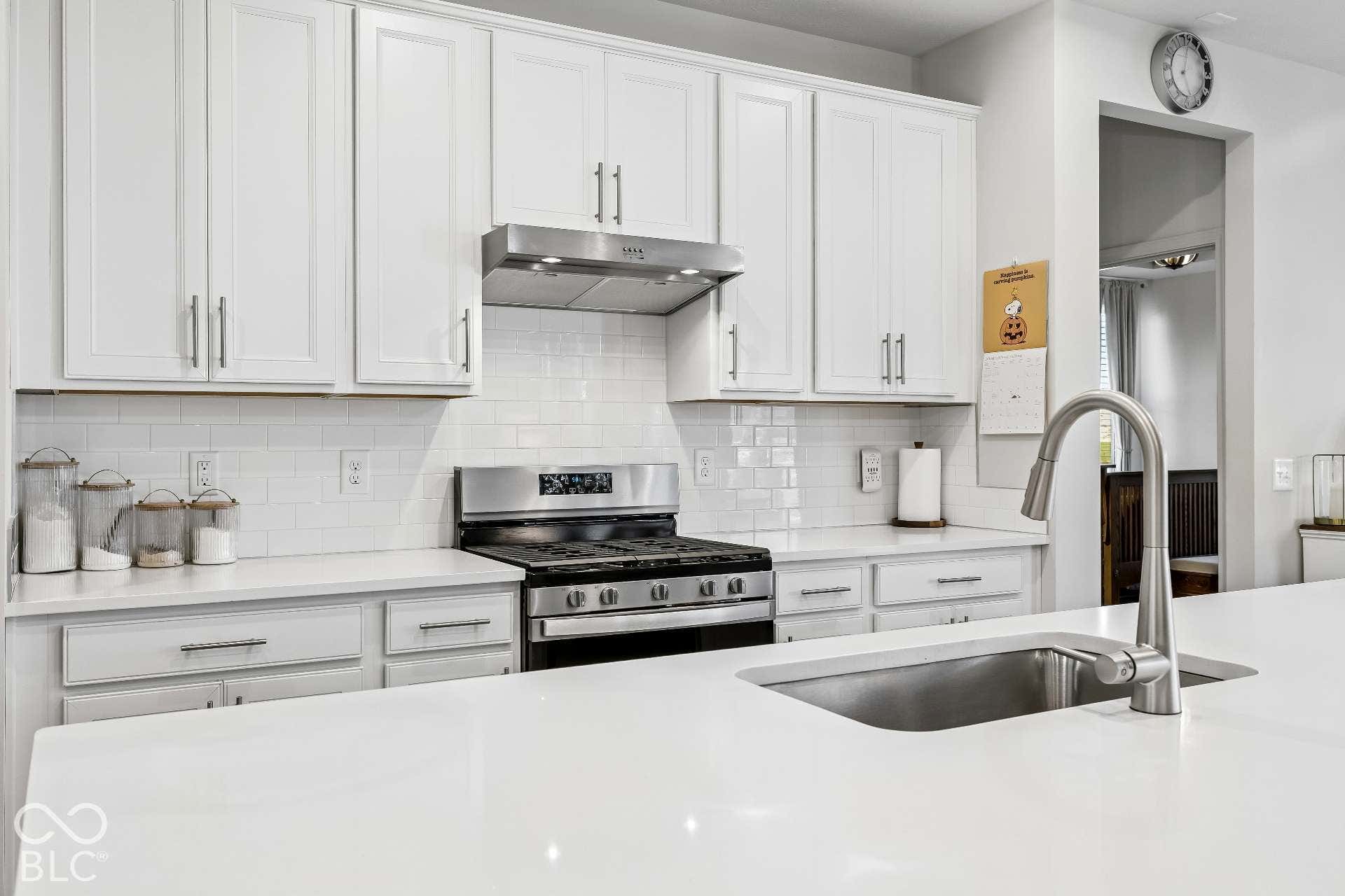 White cabinetry with brushed nickel hardware, subway tile backsplash, stainless steel gas range with coordinating range hood, and a deep stainless steel sink with a gooseneck faucet