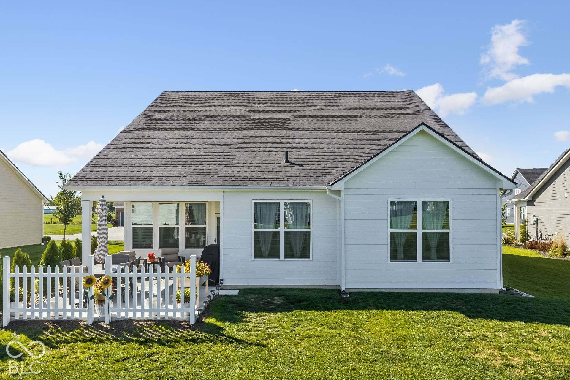 Rear exterior with white siding, covered patio, white picket fence, and dark shingle roof
