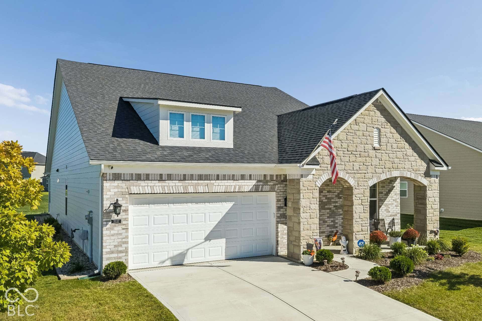 Stone and brick veneer facade with arched entryway, dormer window, attached garage, and a concrete driveway