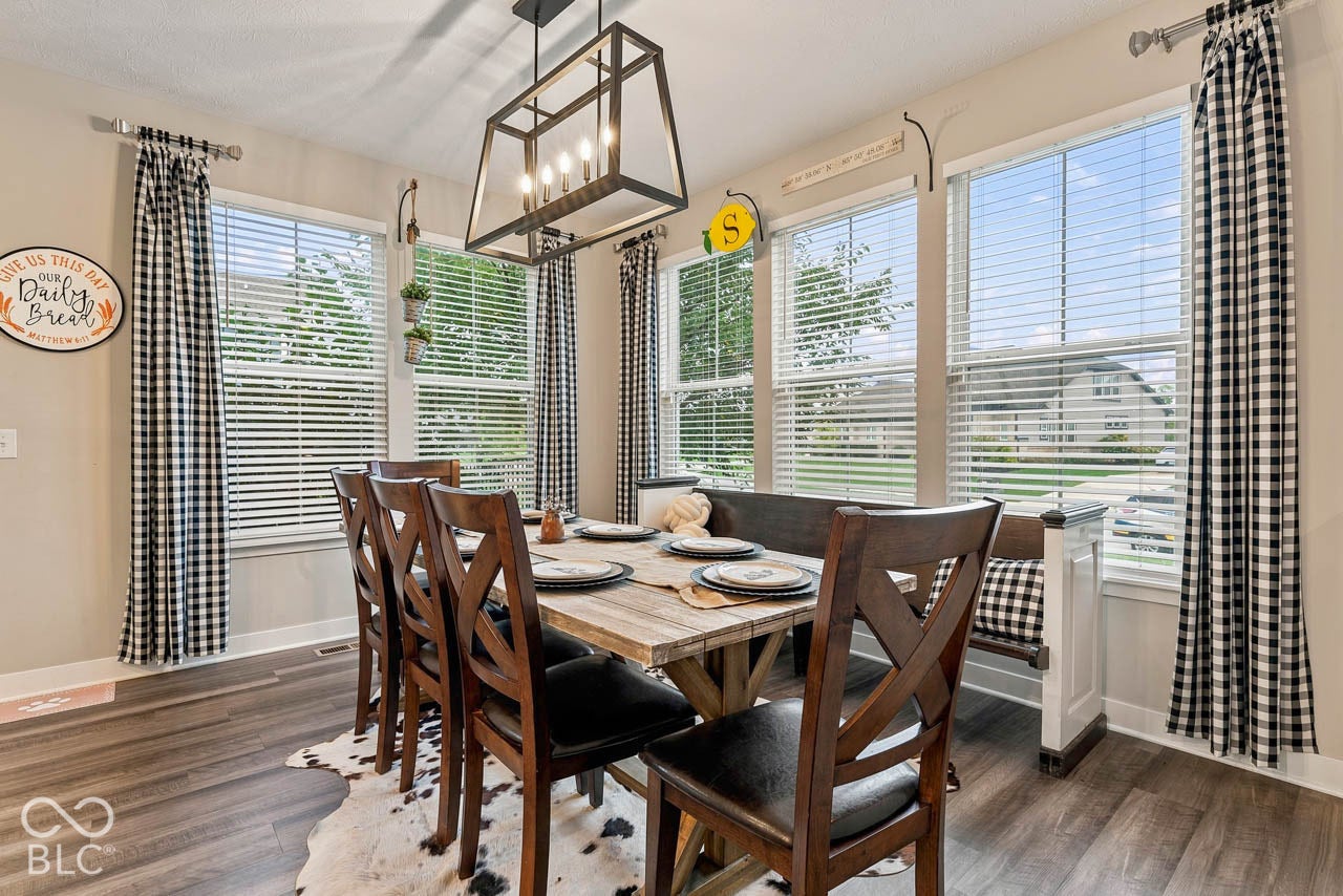 Dining area featuring wood-finish flooring, multiple windows with blinds, and an overhead rectangular chandelier