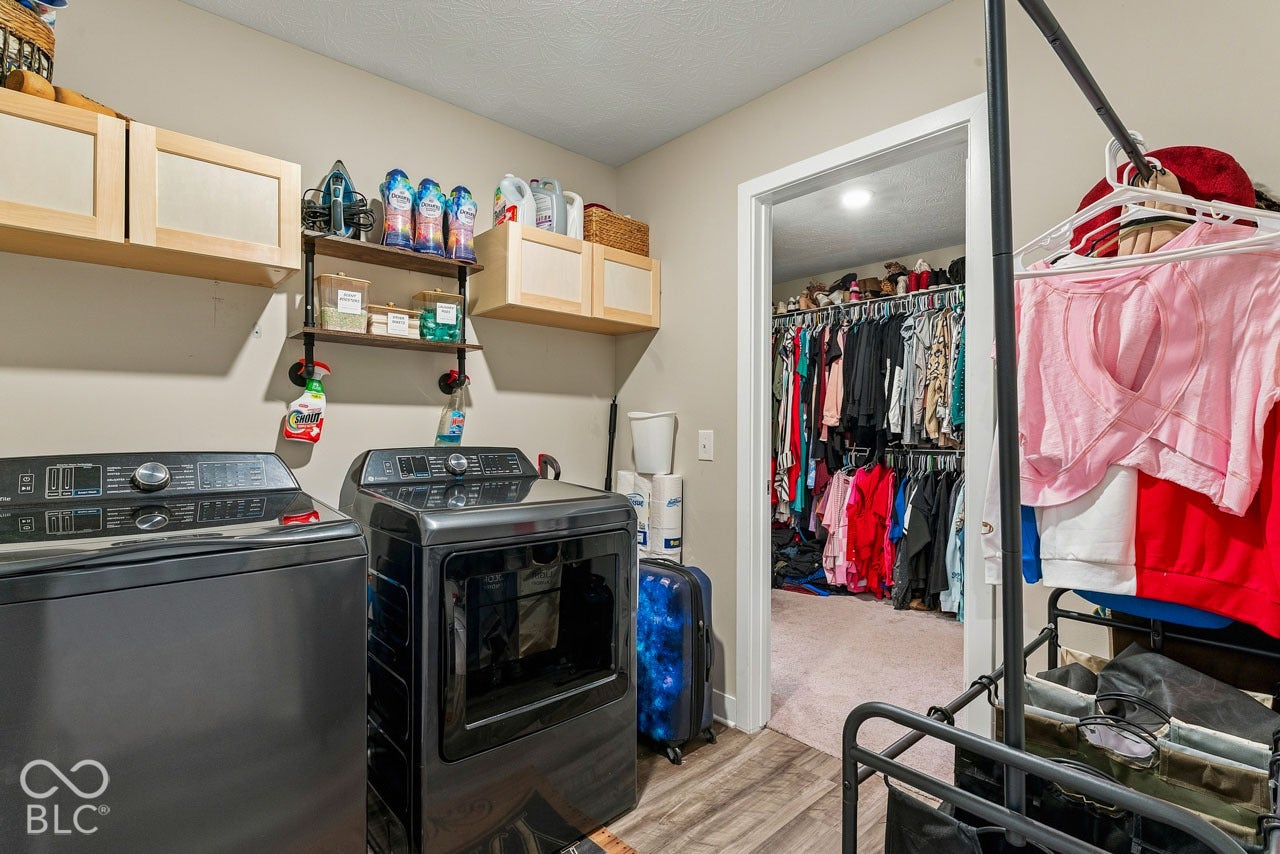 Laundry area featuring wood-finish flooring, overhead cabinetry, and wall-mounted shelving