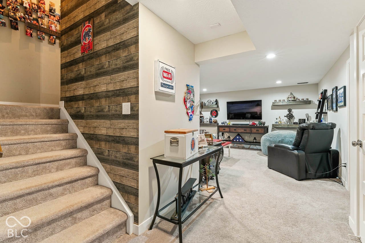 Carpeted stairs leading to a recreation room with recessed lighting, wood-finish accent wall, and built-in shelving