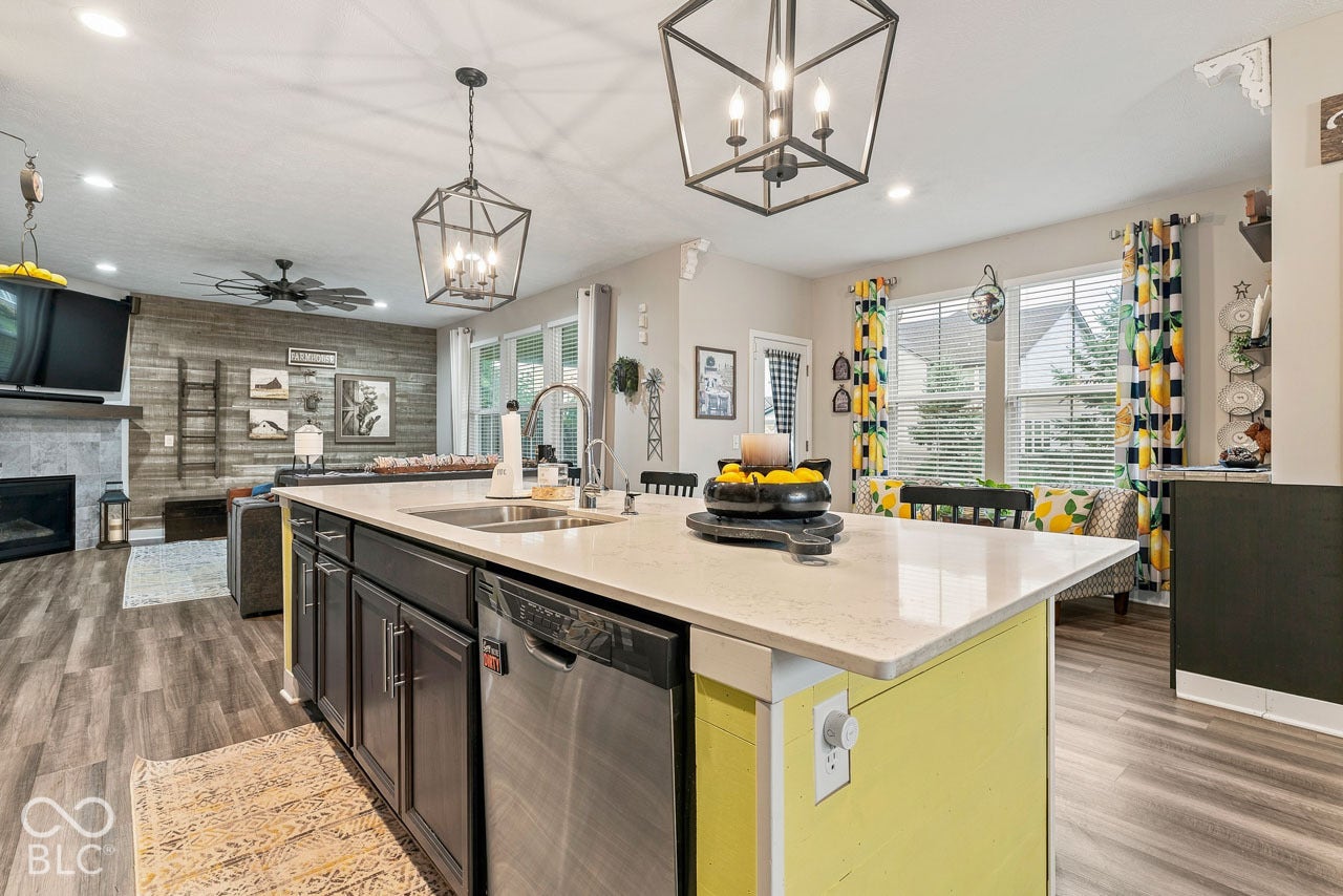 Kitchen island with a light-toned countertop and integrated stainless steel sink, dark cabinetry, and a dishwasher