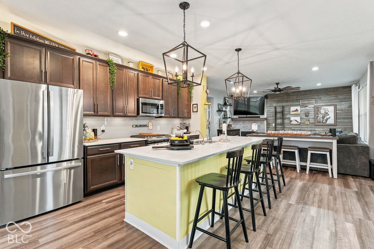 Open-concept living space with wood-finish flooring, a kitchen island with seating, dark wood cabinetry, stainless steel appliances, and a wood-paneled accent wall