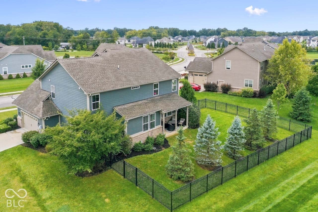 Two-story residence with a covered porch, an attached garage, and a fenced backyard featuring established evergreen trees
