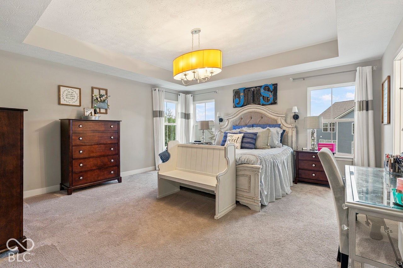 Tray ceiling with recessed lighting, carpeted flooring, and multiple windows providing natural light