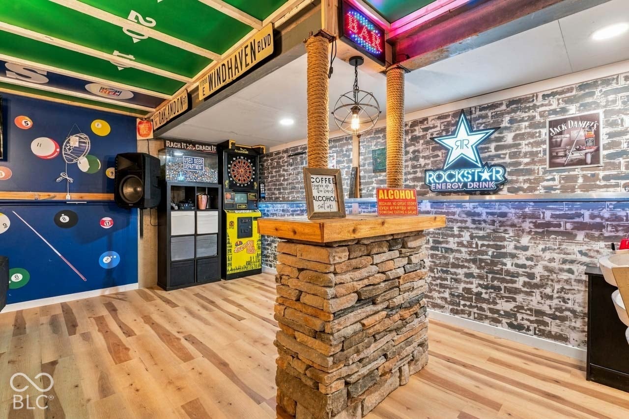 Wood-finish flooring, stone-clad bar with a wood top, exposed ceiling beams, and brick-patterned wall covering