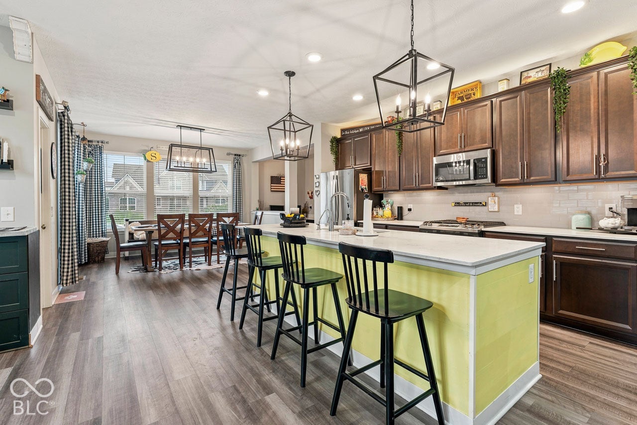 Open-concept kitchen and dining area featuring wood-finish flooring, dark wood cabinetry, a center island with countertop seating, and recessed lighting