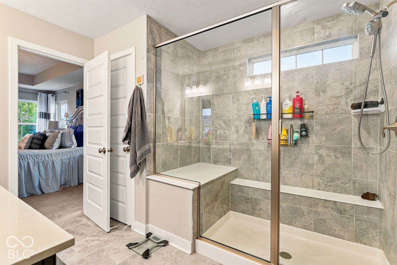Glass-enclosed shower with tile surround, built-in seating, and a fixed showerhead with a handheld sprayer