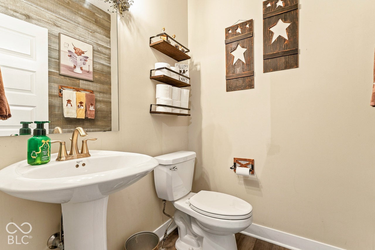 Pedestal sink with brass-finish faucet, built-in wall shelving, and plank-style accent wall