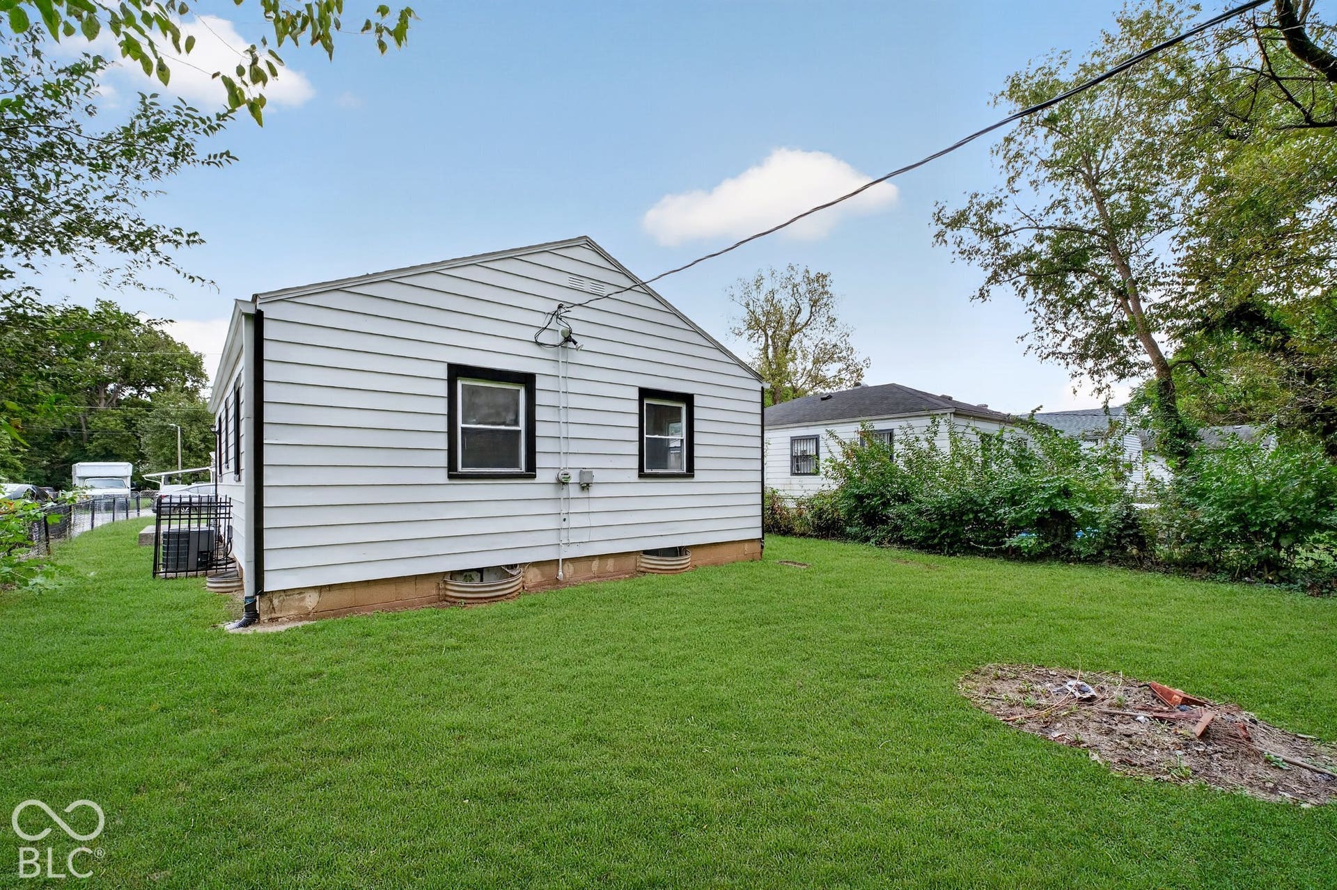 Expansive grass lawn, white horizontal siding exterior, black trim windows, and mature trees