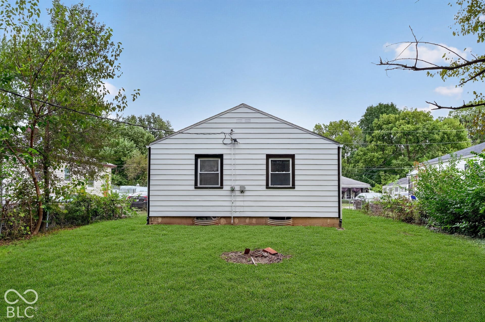 Expansive grassy yard with mature perimeter trees and white horizontal siding