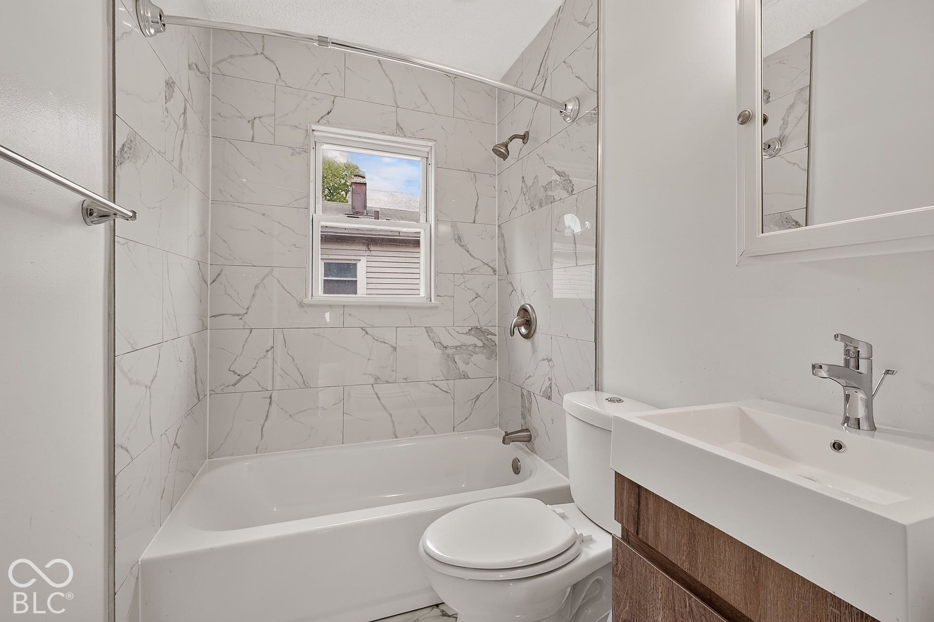 Full bathroom featuring a white bathtub with tile surround, a single-pane window, and a vanity with a rectangular sink and chrome faucet